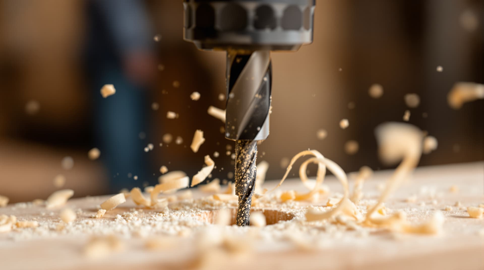 A spade drill bit boring a clean hole through a wooden board with wood shavings curling out